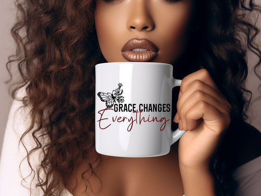 A woman holding a 15oz white ceramic mug with the text 'Grace Changes Everything' printed on it.